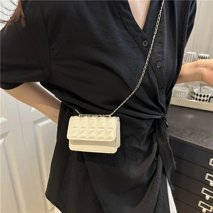 White quilted mini crossbody bag with gold chain strap worn over a black V-neck shirt
