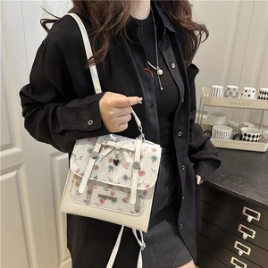 Chic white leather handbag with floral lace overlay and decorative bow handle shown on model