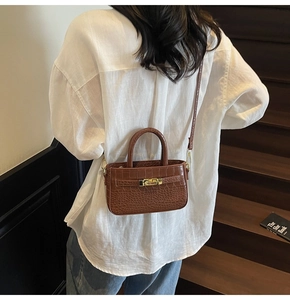 Detail of a brown crocodile texture bag with gold hardware worn on a wooden staircase