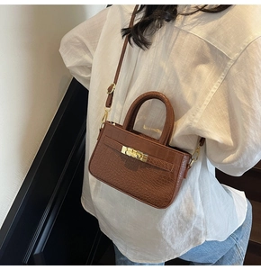 Detail of a brown crocodile texture handbag featuring a classic gold-tone metal twist lock