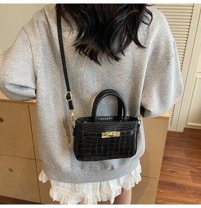 Detail of black crocodile texture bag with gold metal lock and leather shoulder strap