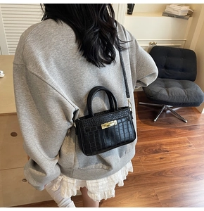 Detail showing glossy black crocodile pattern texture and golden clasp on a crossbody bag