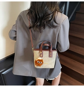 Detail of grey bucket bag with brown handles and plush charm worn as a shoulder bag