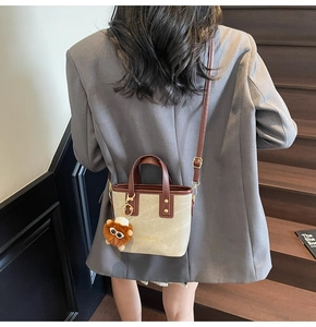 Detail of canvas tote bag with brown leather trim and plush lion charm worn by model