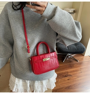 Detail of red crocodile texture handbag with gold twist lock worn as crossbody bag