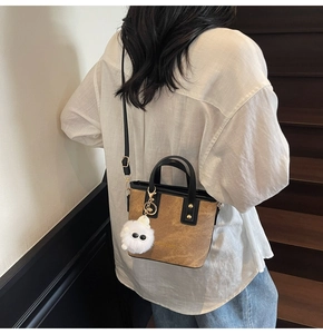 Detail of vintage brown textured PU leather handbag with gold rivets and white plush charm