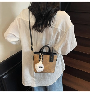 Chic brown leather bucket bag with contrasting black handles and plush charm detail