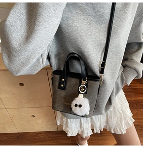 Detail of grey suede handbag with black handles and a white plush pompom charm