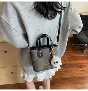 Detail of canvas tote bag with leather straps and white plush pom-pom keychain accessory