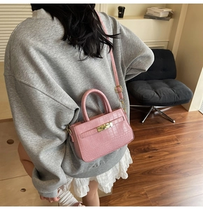 Pink croc-effect small square bag with gold hardware shown on a model's shoulder