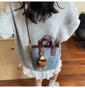 Detail of blue denim bucket bag with brown leather trim and fuzzy eye charm