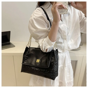 Detail of black snake-embossed leather shoulder bag with gold chain strap and square buckle