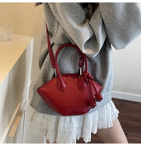 Detailed view of red crescent moon handbag featuring decorative rope knot handles and silver zip