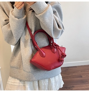 Model wearing a red semi-circle leather crossbody bag with a round handle and knot detail