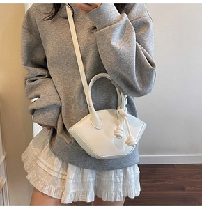 White geometric crossbody bag with knot handle detail styled on a model in casual wear