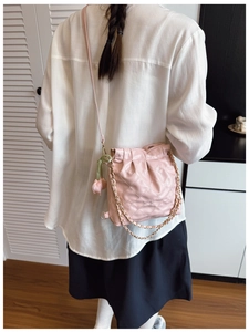 Pink quilted bucket bag detail with gold chain strap and floral charm on a shoulder strap