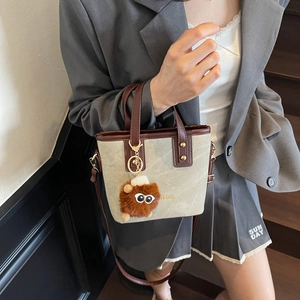 Chic canvas and leather bucket bag with plush charm and adjustable strap for women