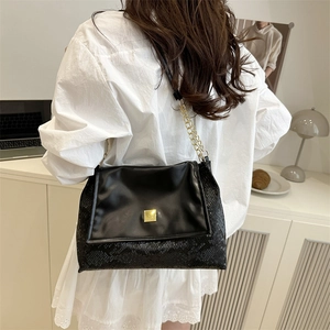 Schwarze Schultertasche mit Schlangenmuster und Goldkette am Modell präsentiert