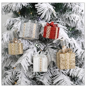 Close-up of glittery Christmas gift box ornaments with lace ribbons on a snowy tree