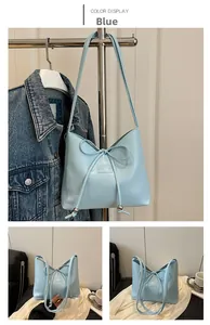 Dettaglio di una borsa a spalla in pelle azzurra con fiocco decorativo e logo impresso