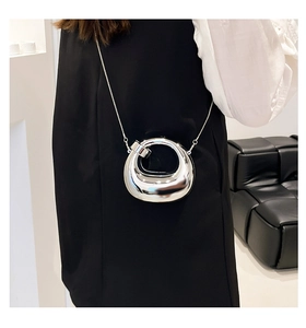 Detail of silver metallic mini bag with oval shape and fine chain strap on model