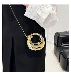 Close-up of golden circular mini crossbody bag with sleek metal texture and fine chain strap