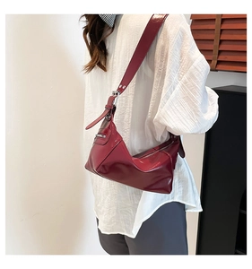 Detailed view of deep red patent leather shoulder bag with wide strap and silver buckle