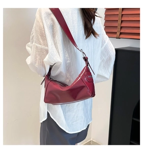Detail of a dark red glossy leather crescent hobo bag with wide shoulder strap