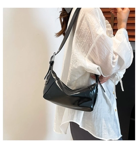 Side view of black patent leather shoulder bag with glossy finish and metal buckles
