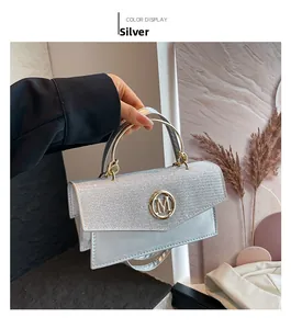 Close-up of a silver glitter handbag with a gold M logo and metallic cylinder handle