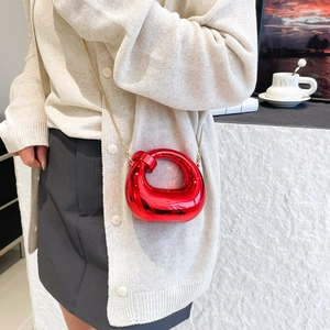 Red metallic circular crossbody bag with gold chain strap worn by model in minimalist setting