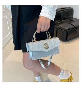 Silver handbag with glitter flap and metallic M logo shown in a lifestyle setting