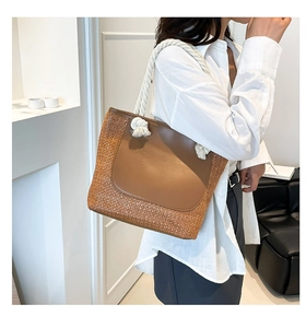 Detail of woven straw tote bag with brown leather panel and white cotton rope handle