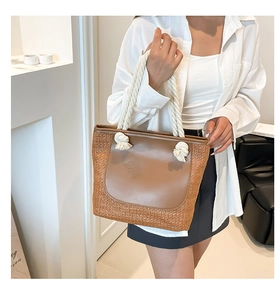 Close-up of woven straw tote bag featuring brown leather patch and white rope handles