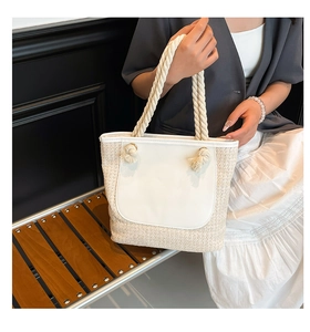 Detail of woven straw tote bag featuring white faux leather panel and knotted handles