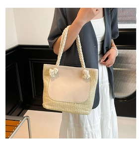 Detail of woven straw tote bag featuring cream leather panel and rope knot handle decoration