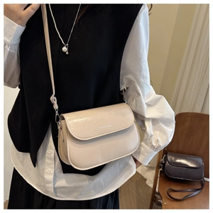Detail van een crèmekleurige crossbodytas met zilveren hardware en verstelbare riem