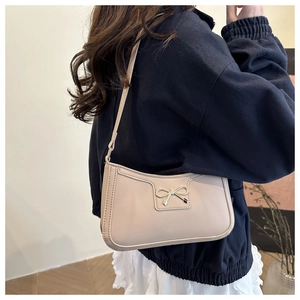 Detail view of cream shoulder bag with golden bow ornament on smooth leather finish