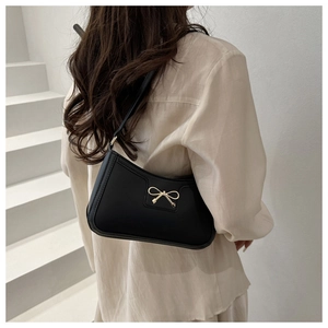 Borsa sottobraccio nera con fiocco dorato indossata da una modella in un set minimalista