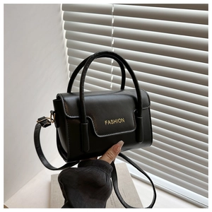Detail einer minimalistischen schwarzen Handtasche mit goldenem Fashion Schriftzug