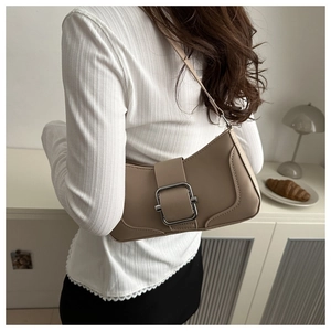 Gros plan d'un sac baguette en cuir beige avec boucle argentée porté à l'épaule