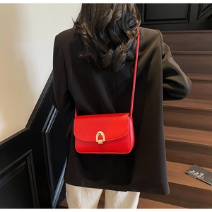 Detailed view of red leather saddle bag featuring a stylish gold U-shaped metal buckle clasp