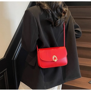 Close-up of a red leather flap shoulder bag featuring a gold U-shaped metal buckle on the front