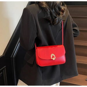 Red leather shoulder bag with gold hardware worn by model on dark wooden stairs