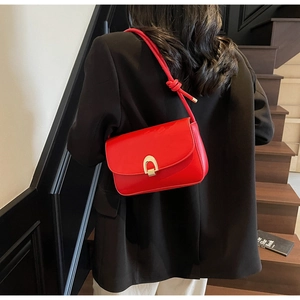 Detail view of red leather shoulder bag featuring a gold horseshoe buckle and knotted strap