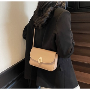 Detail of beige shoulder bag with golden horseshoe buckle on model in black blazer