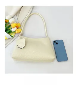 Detail showing cream faux crocodile texture shoulder bag next to a mobile phone