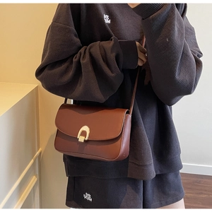Side view of model wearing a vintage brown matte leather crossbody saddle bag with gold buckle