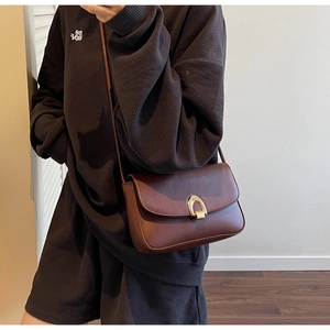 Detail of dark brown leather shoulder bag featuring a gold horseshoe metal buckle