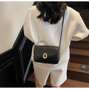 Detail of minimalist black leather crossbody bag with elegant gold horseshoe clasp
